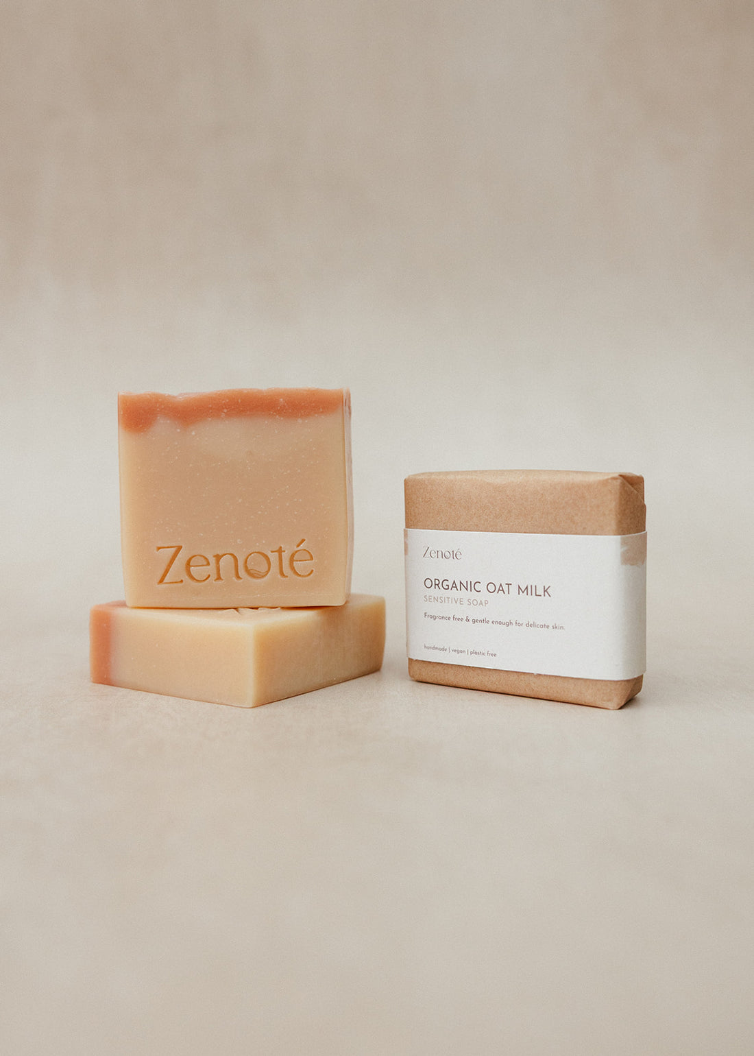 2 White soaps with pink topping, one lying flat and the second balanced on top. A third stop is packaged in brown paper with a white band detailing the product information. 