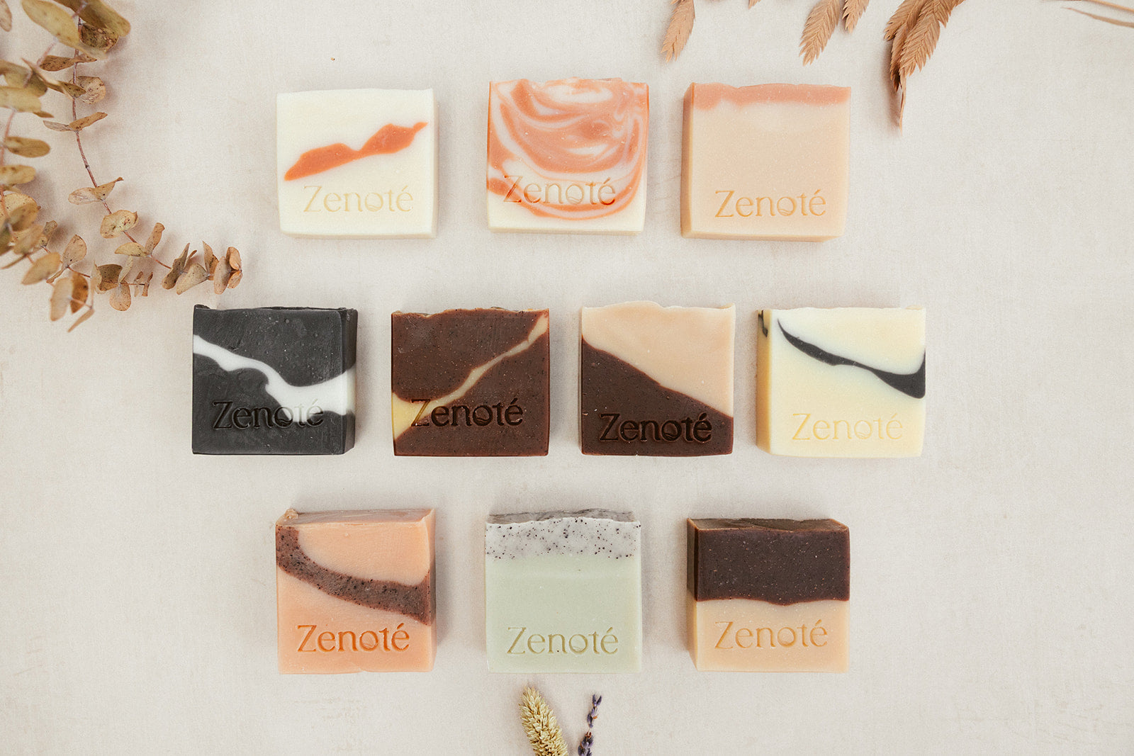 Flat Lay Image of 10 Natural Soap Bars. 3 bars at the top, 4 bars in the middle and 3 at the bottom. Luxary  Soap shades range from pastels though to dark with eye-catching designs and the word Zenoté stamped into each bar.